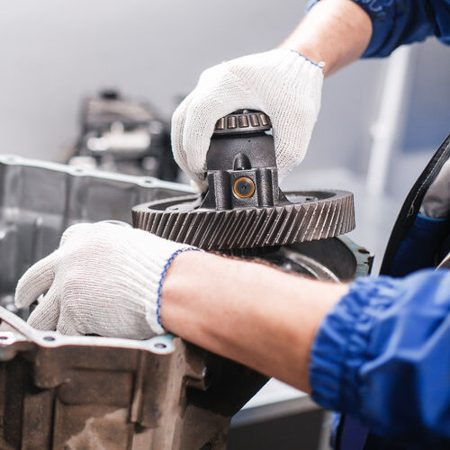 Close-up of hands working on a car transmission.